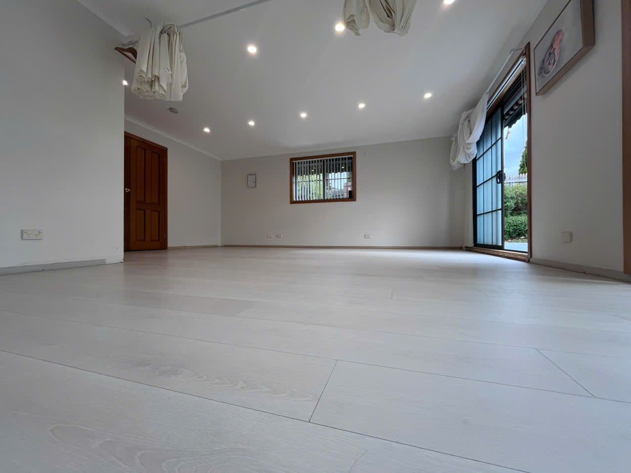 Pale whitewashed oak-look laminate planks across a freshly painted, empty living room.