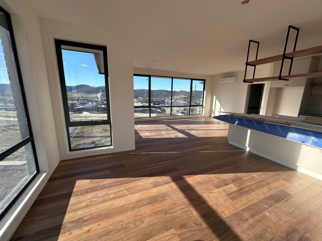 Natural Tasmanian timber floor in a sunlit new build living area, hills visible through the corner windows.